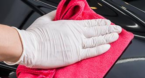 A person in white gloves is wiping a red cloth on a car.