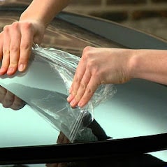 A person is putting a piece of plastic on the hood of a car.