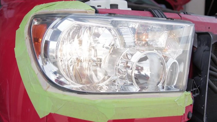 The headlight of a red truck is repaired with tape.