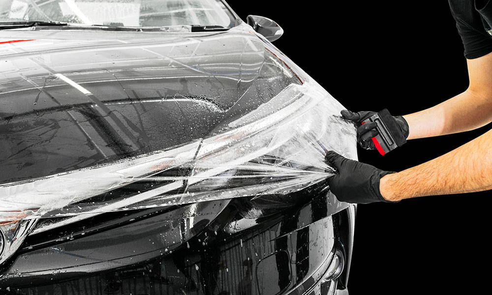 A man is wrapping the hood of a black car.
