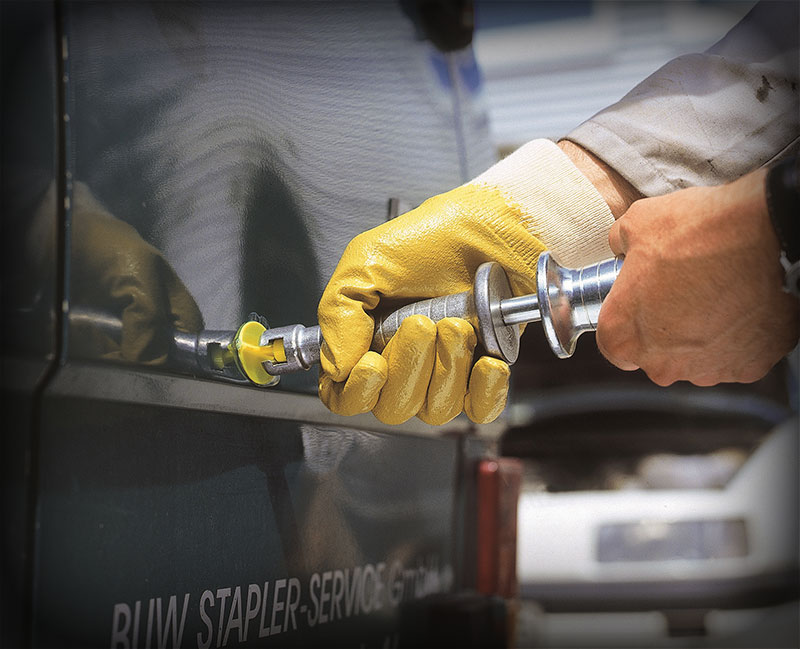 A person in a pair of yellow gloves is putting a screw into a car door.