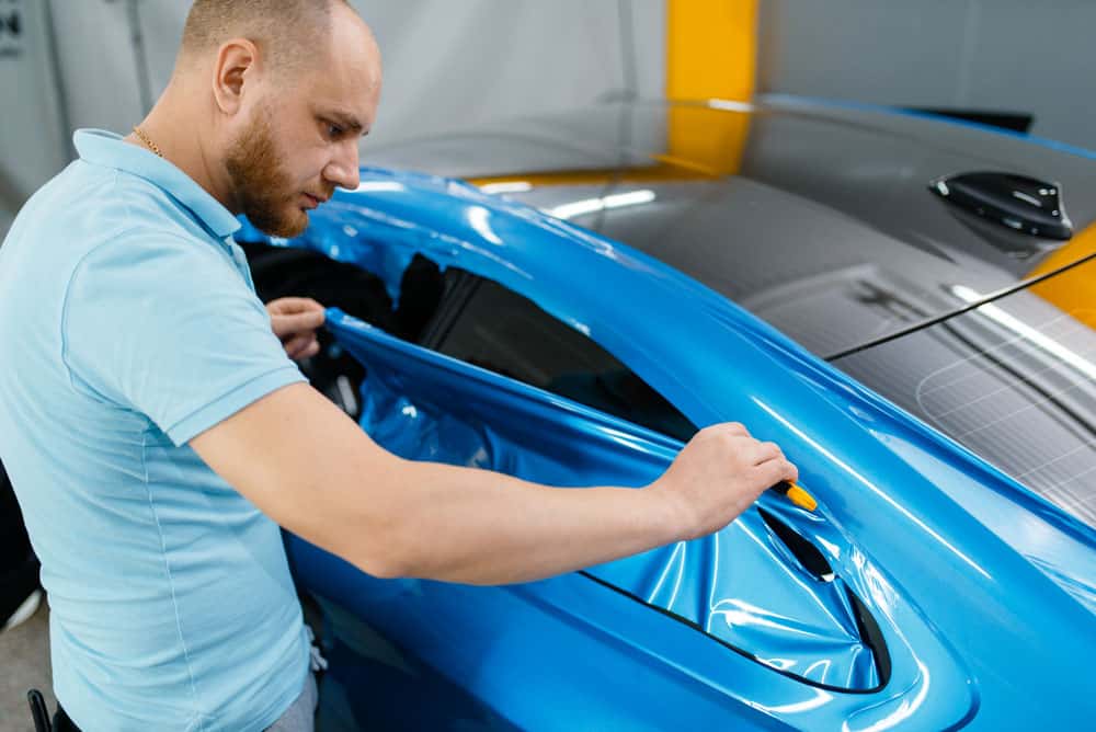 A man is painting a blue car in a garage.