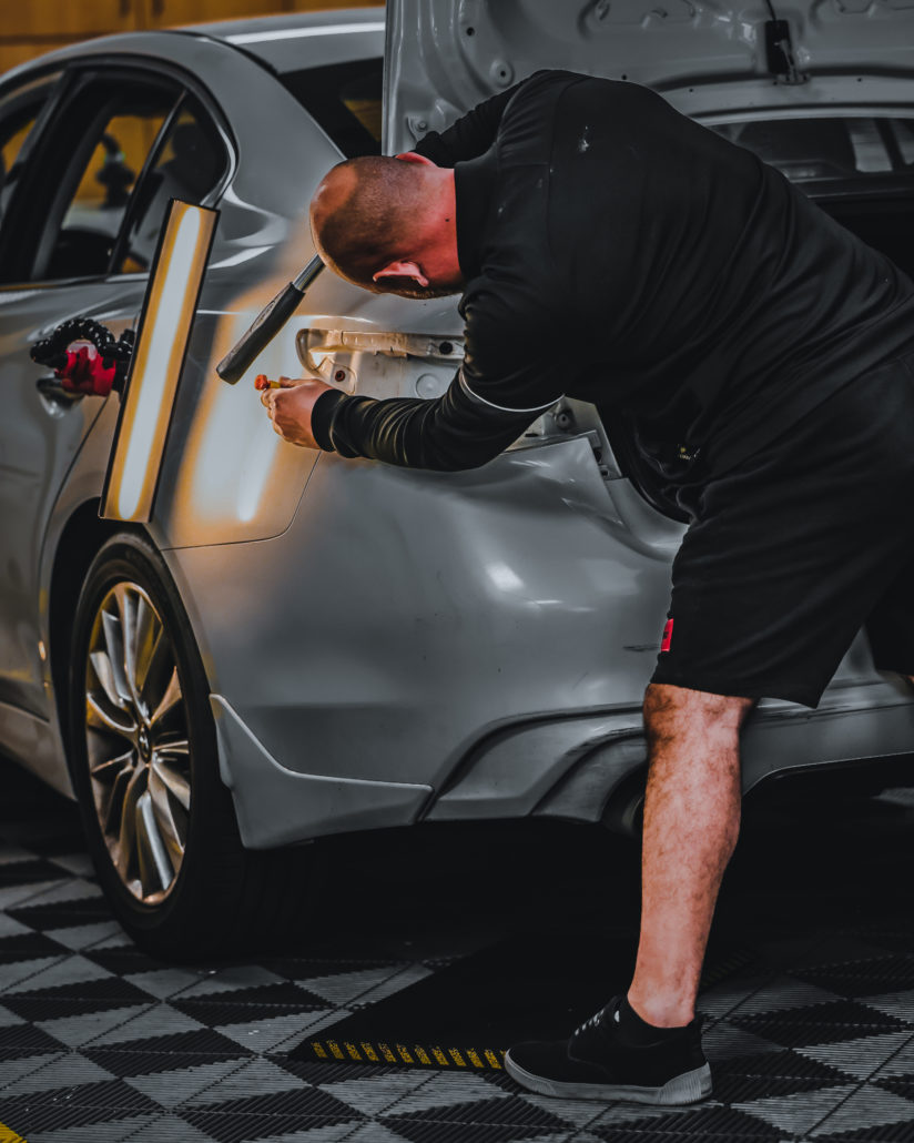 A man training at a PDR Training School working on a silver car in a garage.
