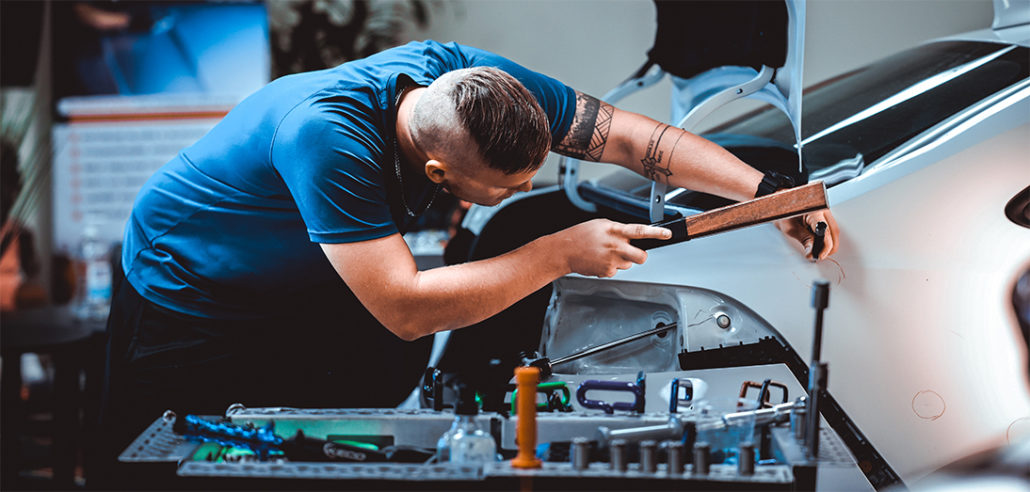 A man receiving paintless dent repair training in a garage.