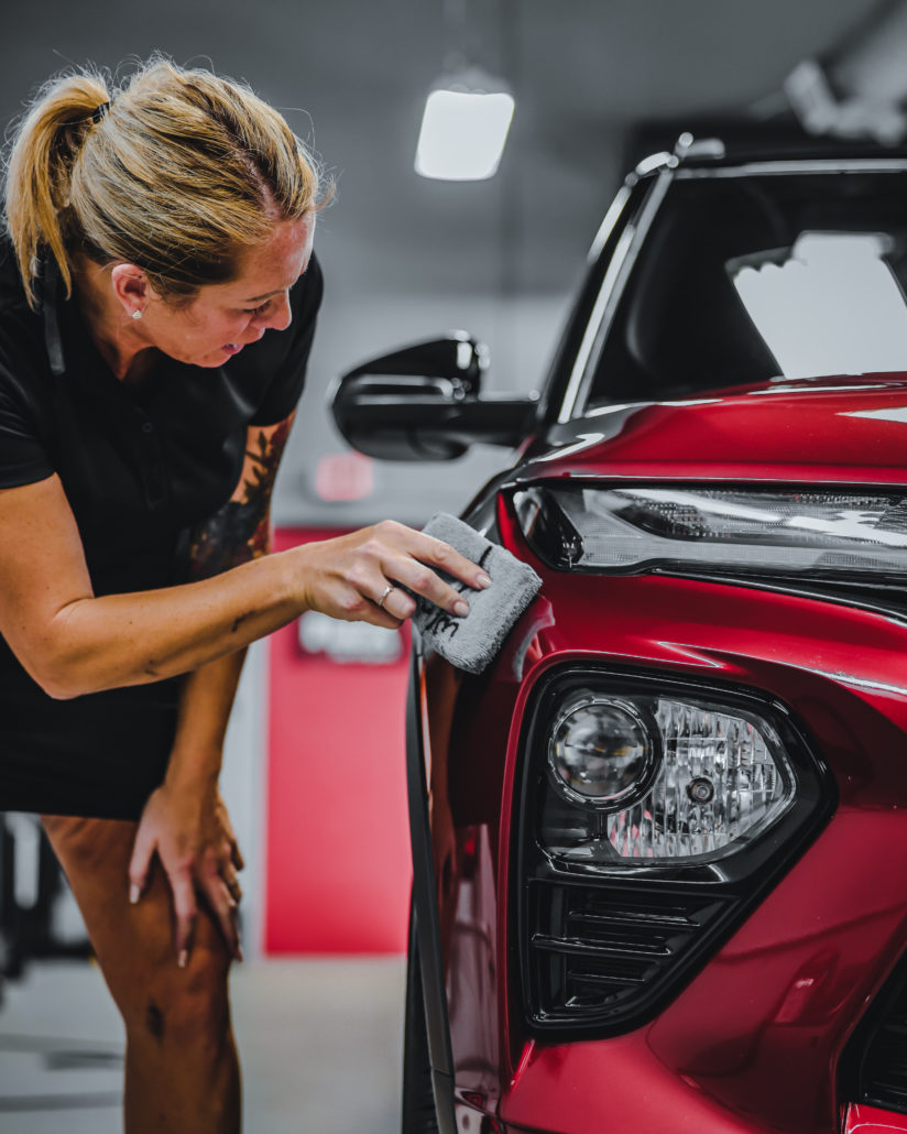 A woman applying ceramic coating to the hood of a red Toyota RAV4.
