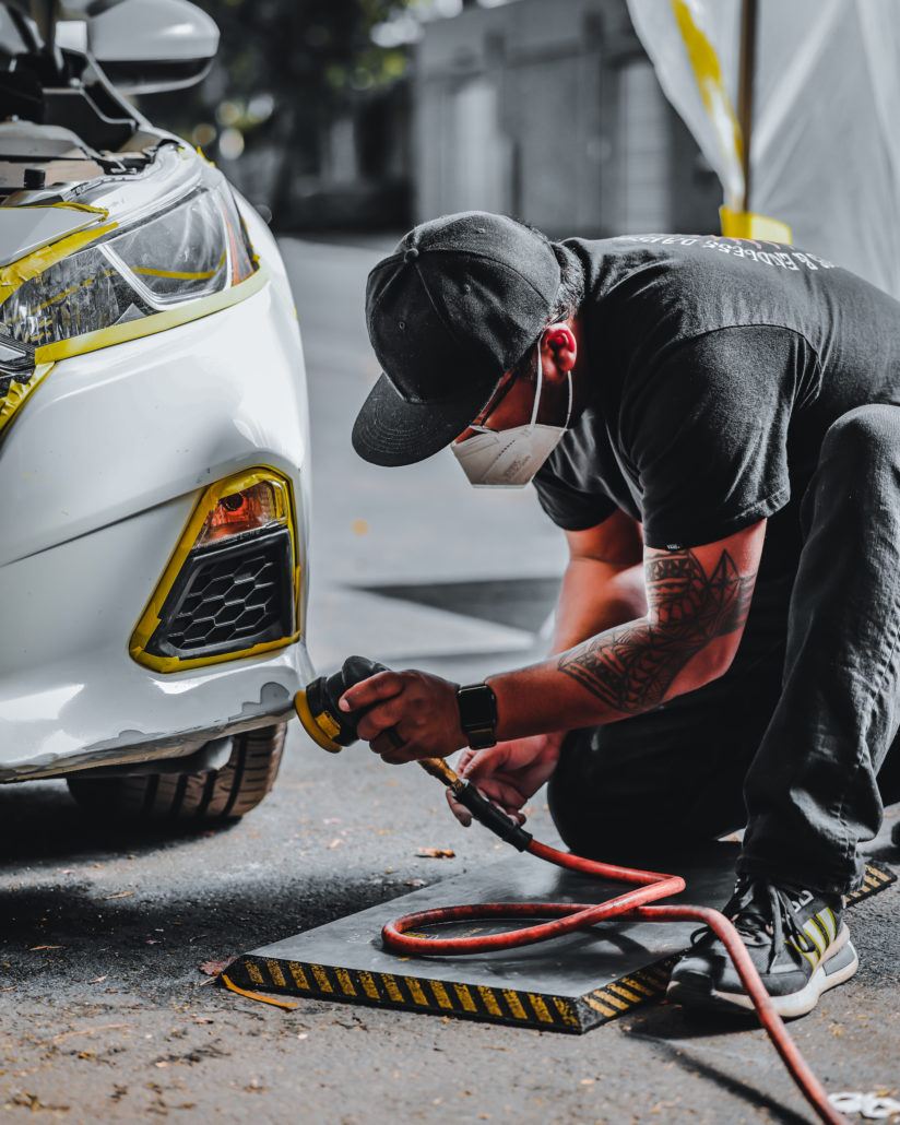 A man in a mask is repairing a car's bumper.