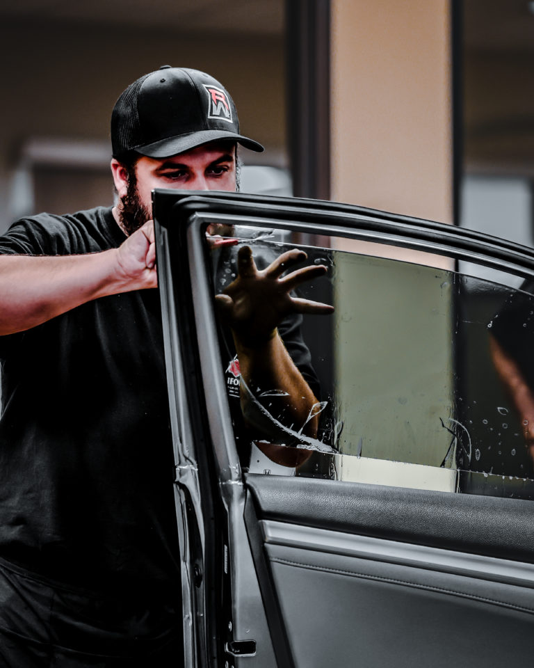 A man opening the door of a car with window tinting.