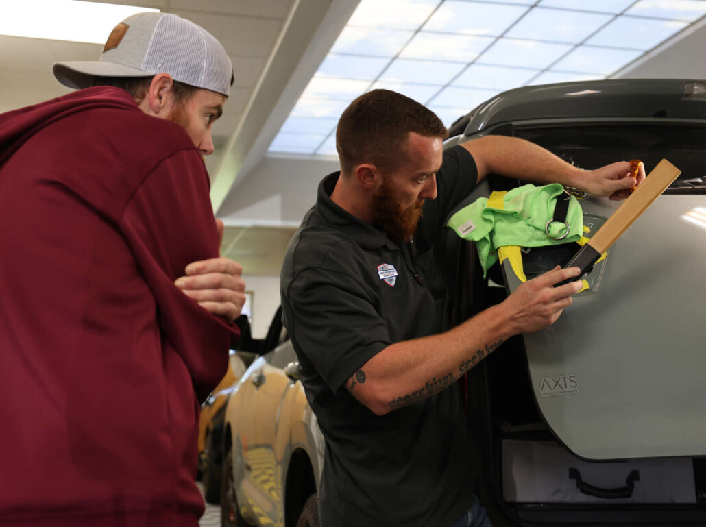 Two individuals from Colorado Dent Repair inspecting or working on the rear of a vehicle, with one using a tool and the other observing.