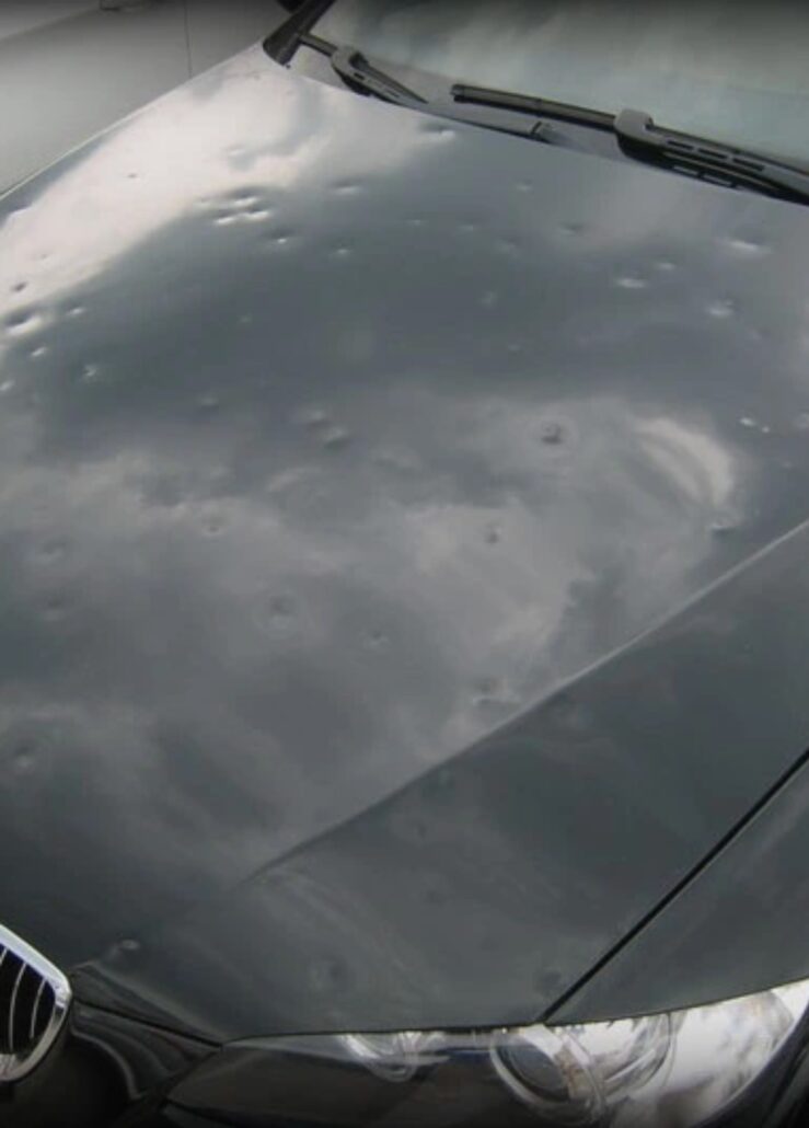 A car hood displaying multiple dents, likely from hail damage, awaits attention at an auto body shop.