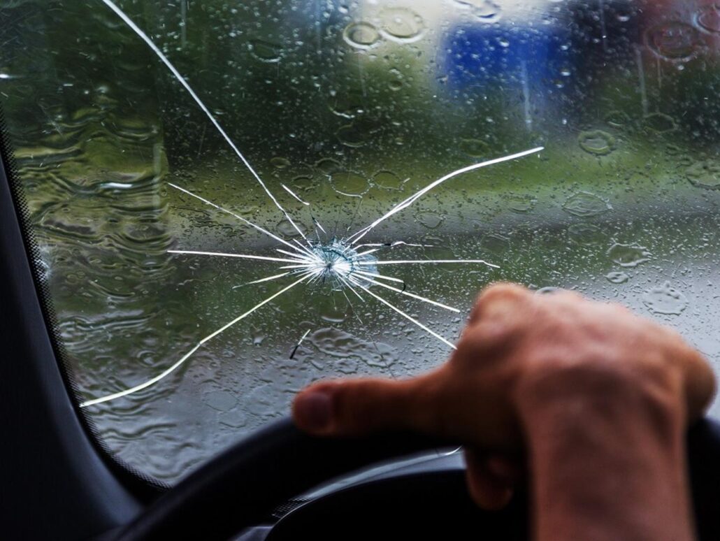 Close-up of a person driving in the rain, their eyes focused on the road through a cracked windshield, protected by a PPF guard.