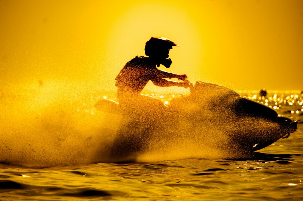 Silhouette of a person riding a jet ski on water during sunset, with water spray illuminated by the golden light, embodying the perfect marine adventure.