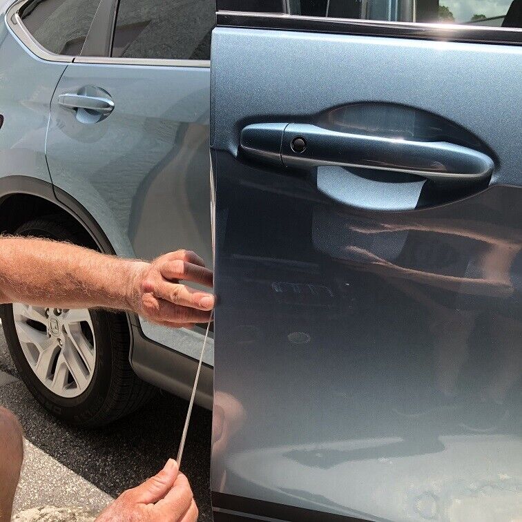 A person is adjusting the alignment of two car door panels, checking the space with a thin tool. The car is light blue, and the detail focuses on the door handle area, ensuring there's no damage to the PPF during this meticulous process.