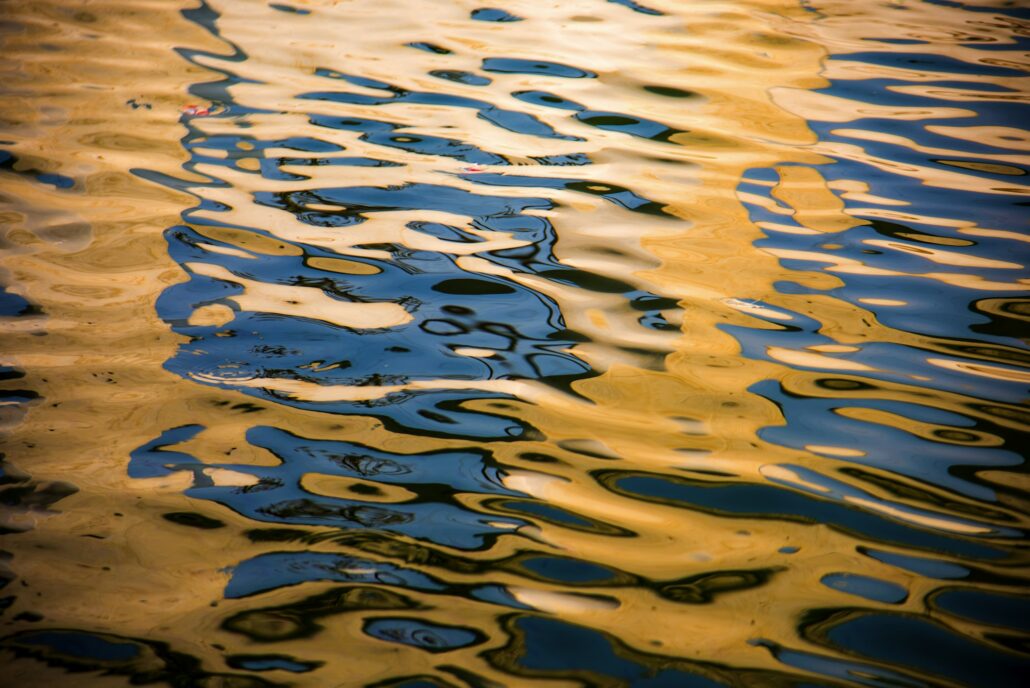 Abstract view of water surface reflecting golden and blue hues, creating rippling patterns reminiscent of marine paint protection film.