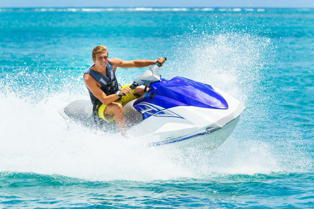 A person in a life jacket is riding a white and blue jet ski on a clear blue ocean with splashes of water around, showcasing the marine adventure in all its glory.