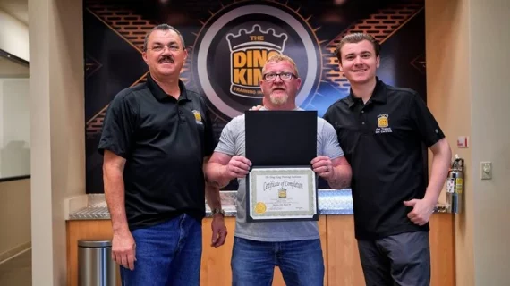 Three men completing Paintless Dent Removal Training, proudly holding their certificate in front of a sign.
