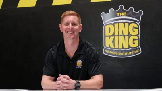 A man participating in paintless dent removal training at a table with the ding king logo.