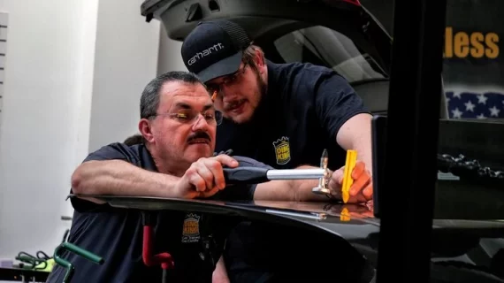 Two men receiving paintless dent removal training in a garage.