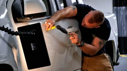 A man with paintless dent removal training is using a tool to open the door of a truck.