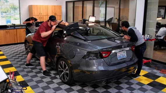 Two men training in paintless dent removal techniques while working on a car in a garage.
